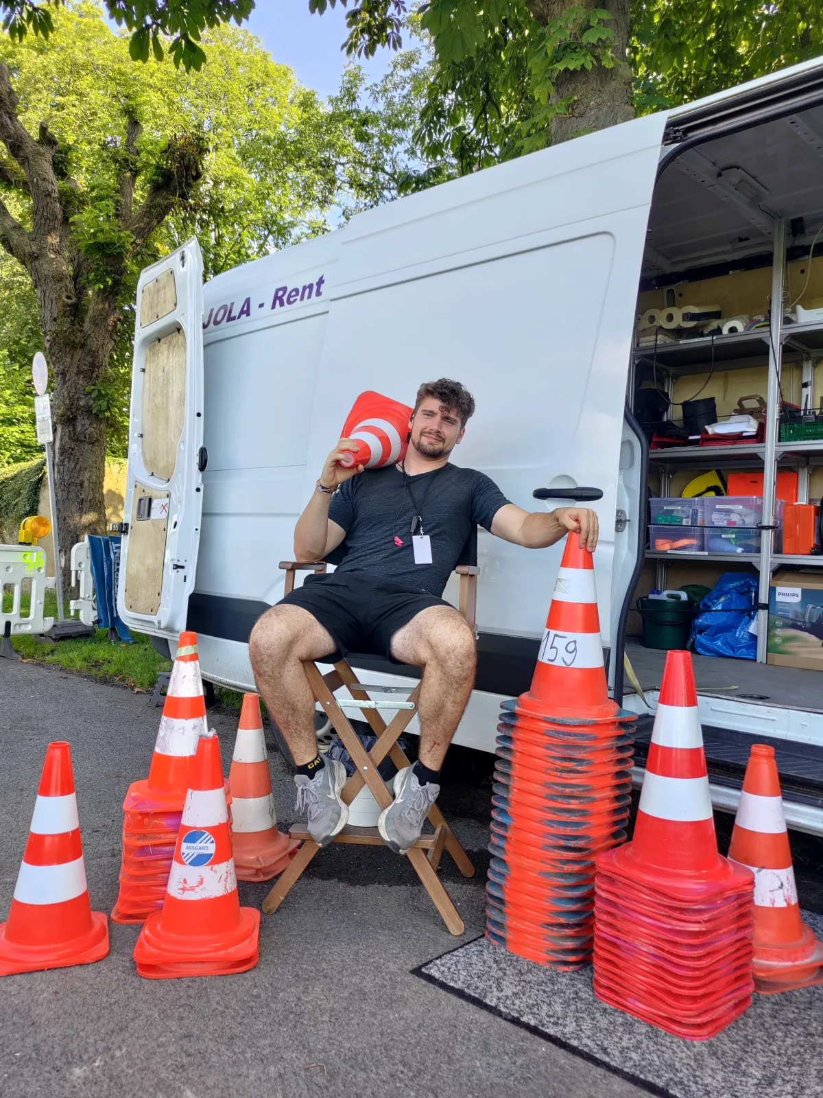 Milan Bourbeck im Regiestuhl zwischen Pylonen vor einem Transporter